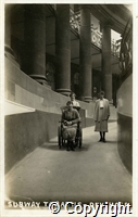 Postcard featuring a black and white photograph of a patient in a bathchair being wheeled down the ramp into the baths at the Devonshire Hospital in Buxton